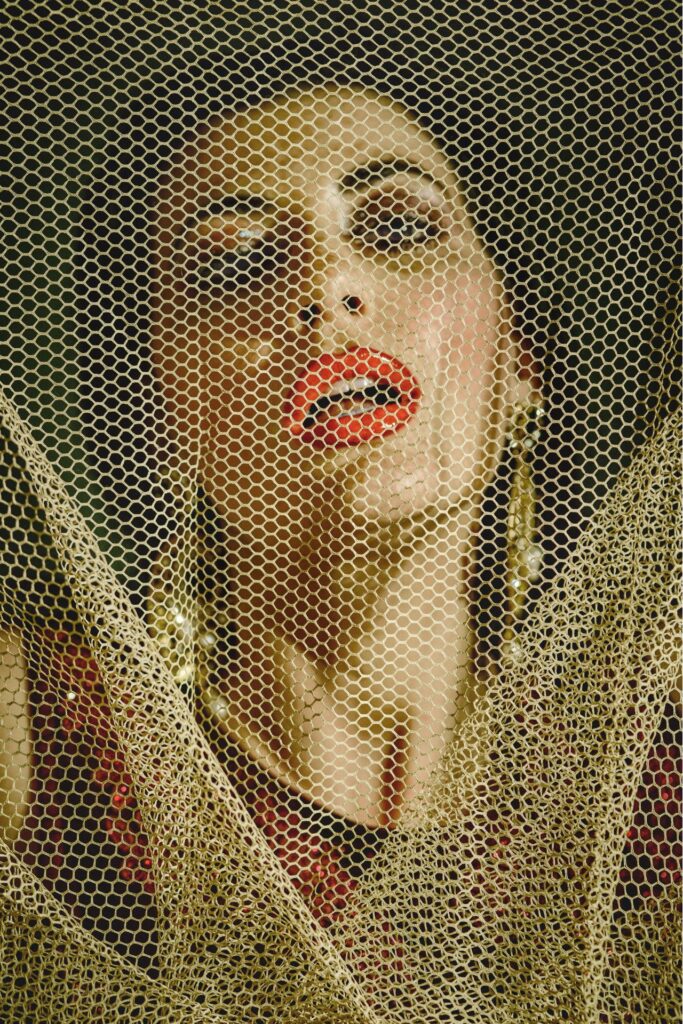 Frau mit rotem Lippenstift steht hinter Netzvorhang