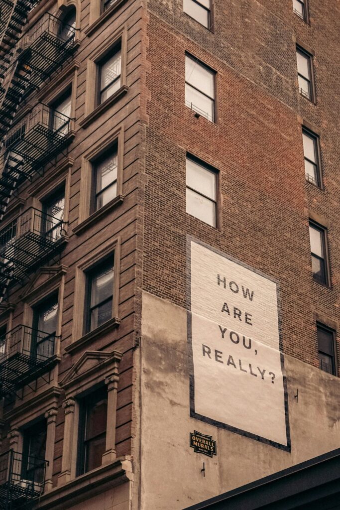 Symbolbild für Mental Load: Plakat auf Hauswand mit "Wie geht es dir wirklich?" 