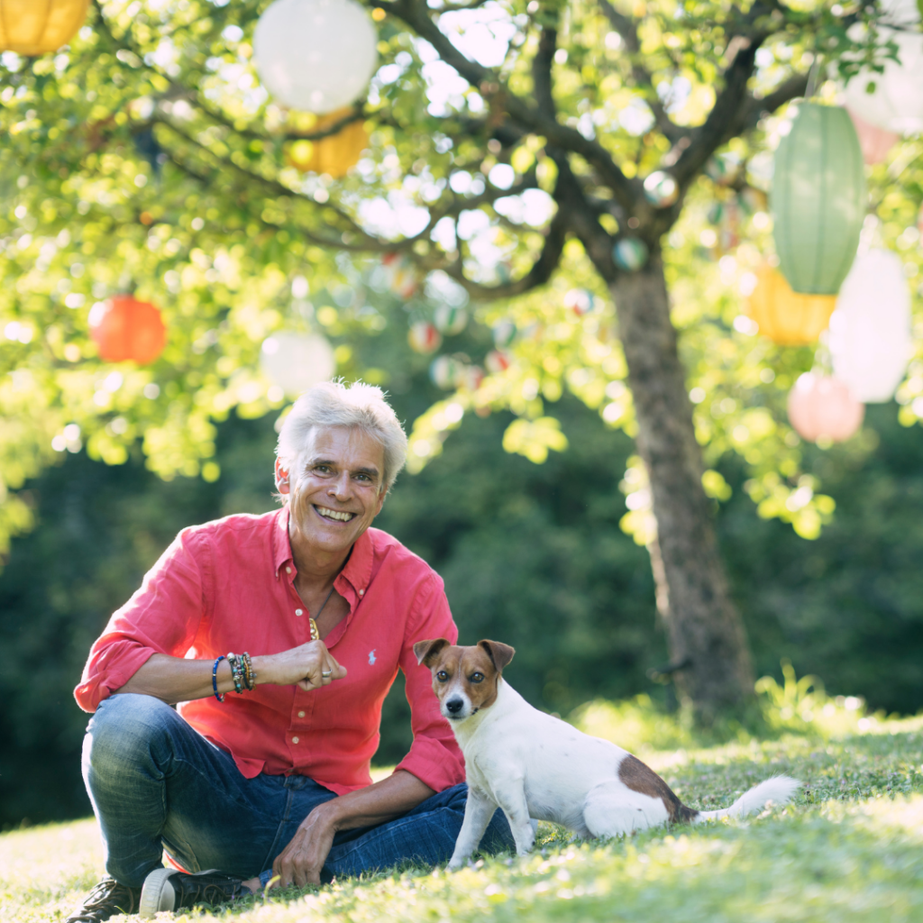 Thomas Brezina im Garten hockend, daneben sein Hund Joppi, im Hintergrund ein Baum mit Lampions