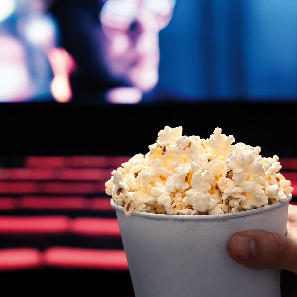 Feminist*innen-Tipps: Hand hält Popcorn im Kinosaal