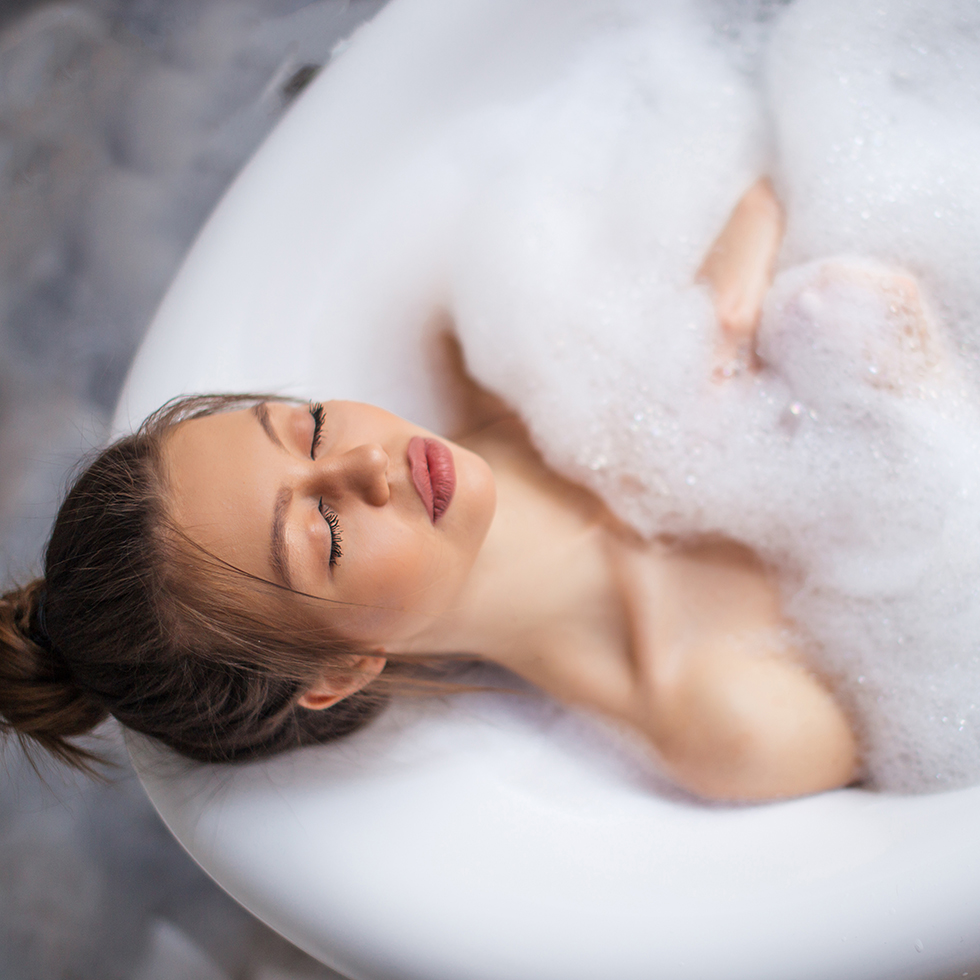 Mom Lifehacks: Junge Frau liegt mit geschlossenen Augen in der Badewanne und entspannt sich