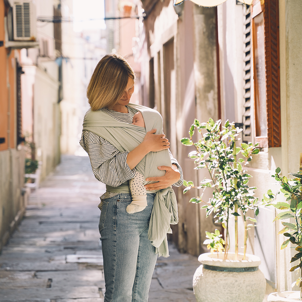 Mom Lifehacks: Mutter trägt Baby in einem Tragetuch durch die Stadt