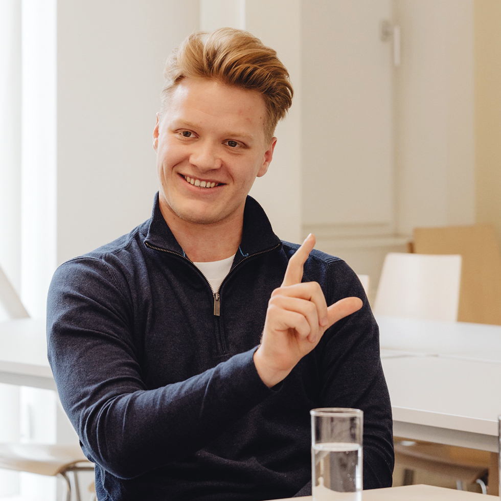 Portrait eines jungen Mannes der lächelt und den Zeigefinger hochhält