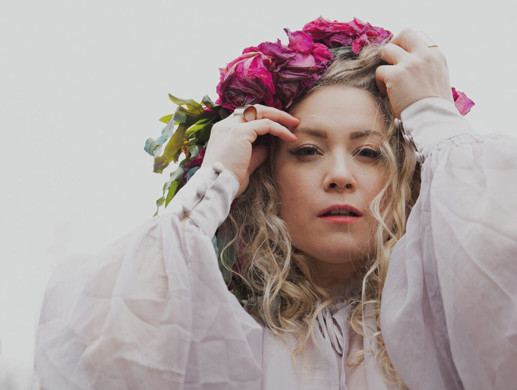 Maria Radutu: blonde Frau mit Blumenkranz in den Haaren und weißer Bluse