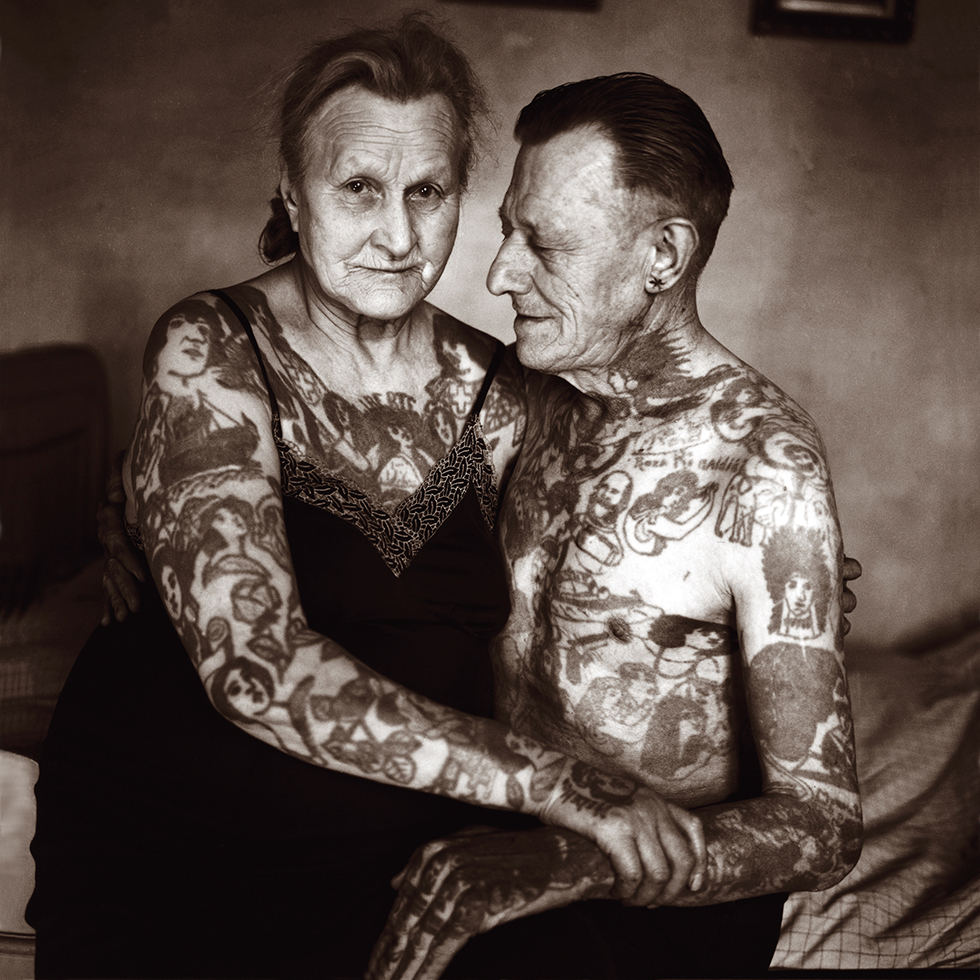 Kulturtipps: Foto in sepia – eine voll-tätowierte alte Frau sitzt am Schoß eines voll-tätowierten Mannes dessen Oberkörper nackt ist