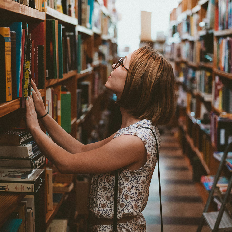 Bücher: Frau steht vor einem großen Bücherregal