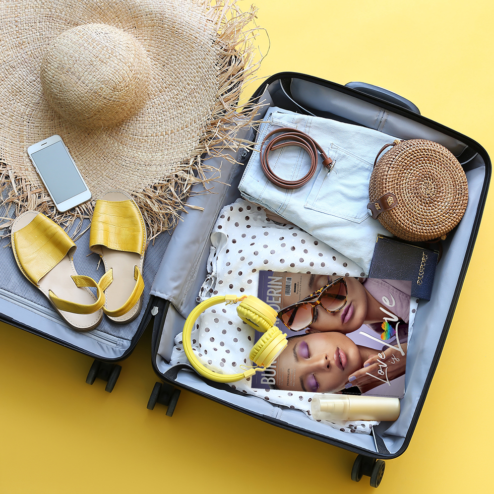 Koffer Packen: gepackter Koffer mit Strohhut, Schuhen, gelben Over-Ear-Kopfhörern, Magazin