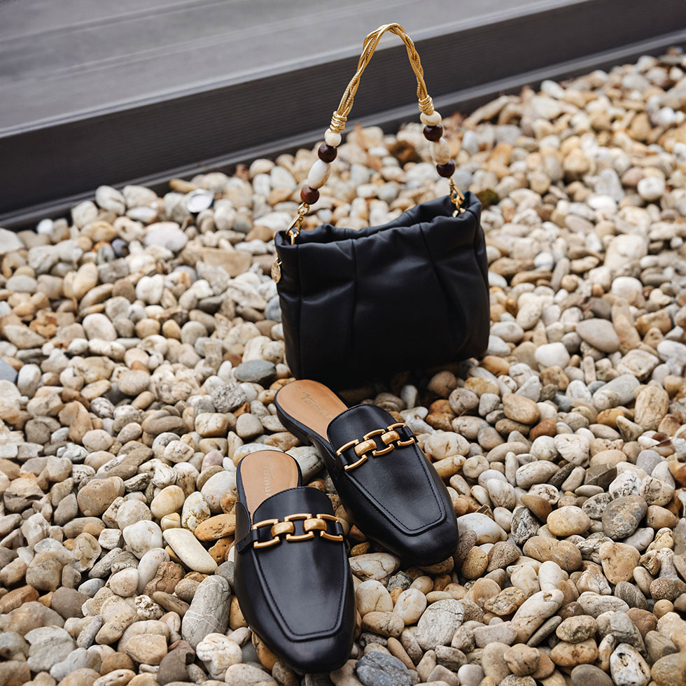 Schwarze Slip-ons und passende schwarze Tasche auf Kieselsteinen