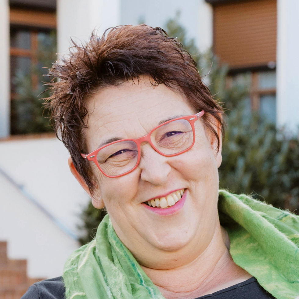 Kurzhaarige ältere Frau mit roter Brille lacht in die Kamera – ein Portrait