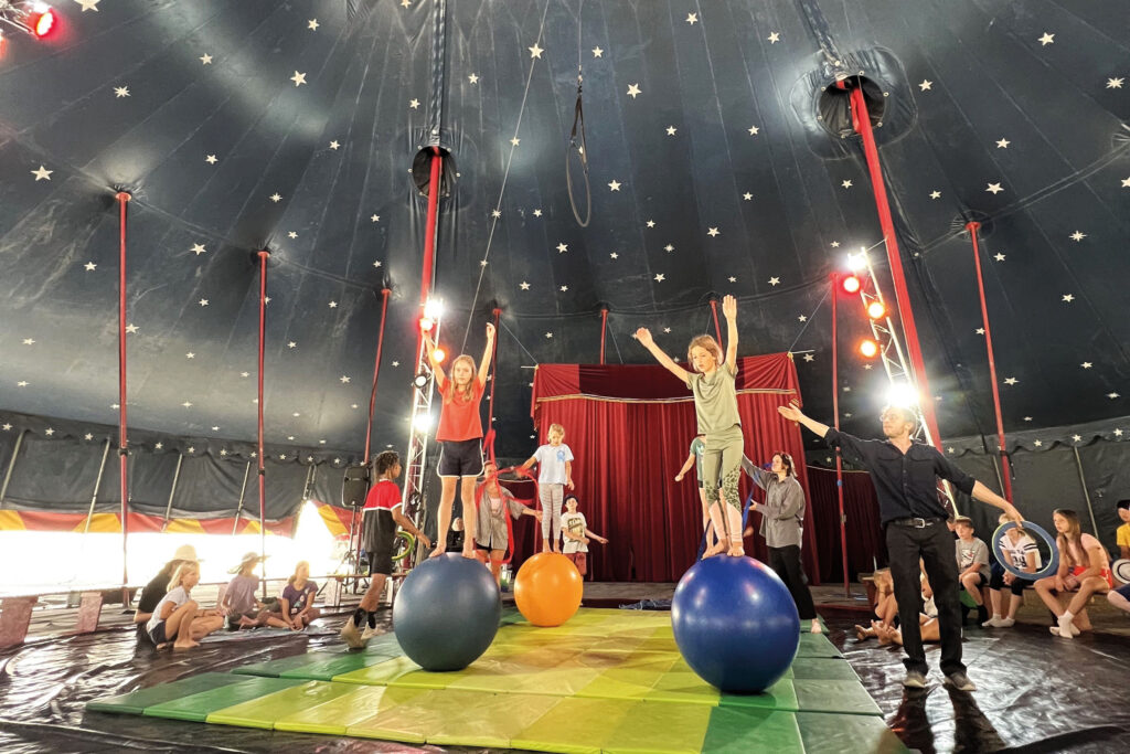 Cirkusglück: Kinder auf großen Bällen balancierend in einer Zirkusarena