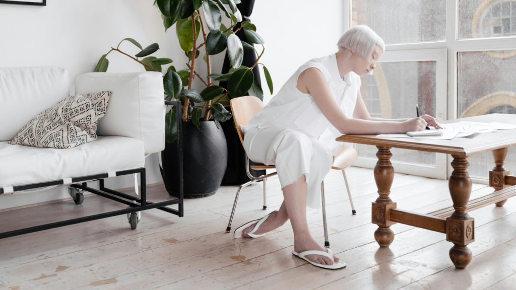 Eine Frau in weiß gekleidet trägt weiße Fliflops und sitz an einem Schreibtisch