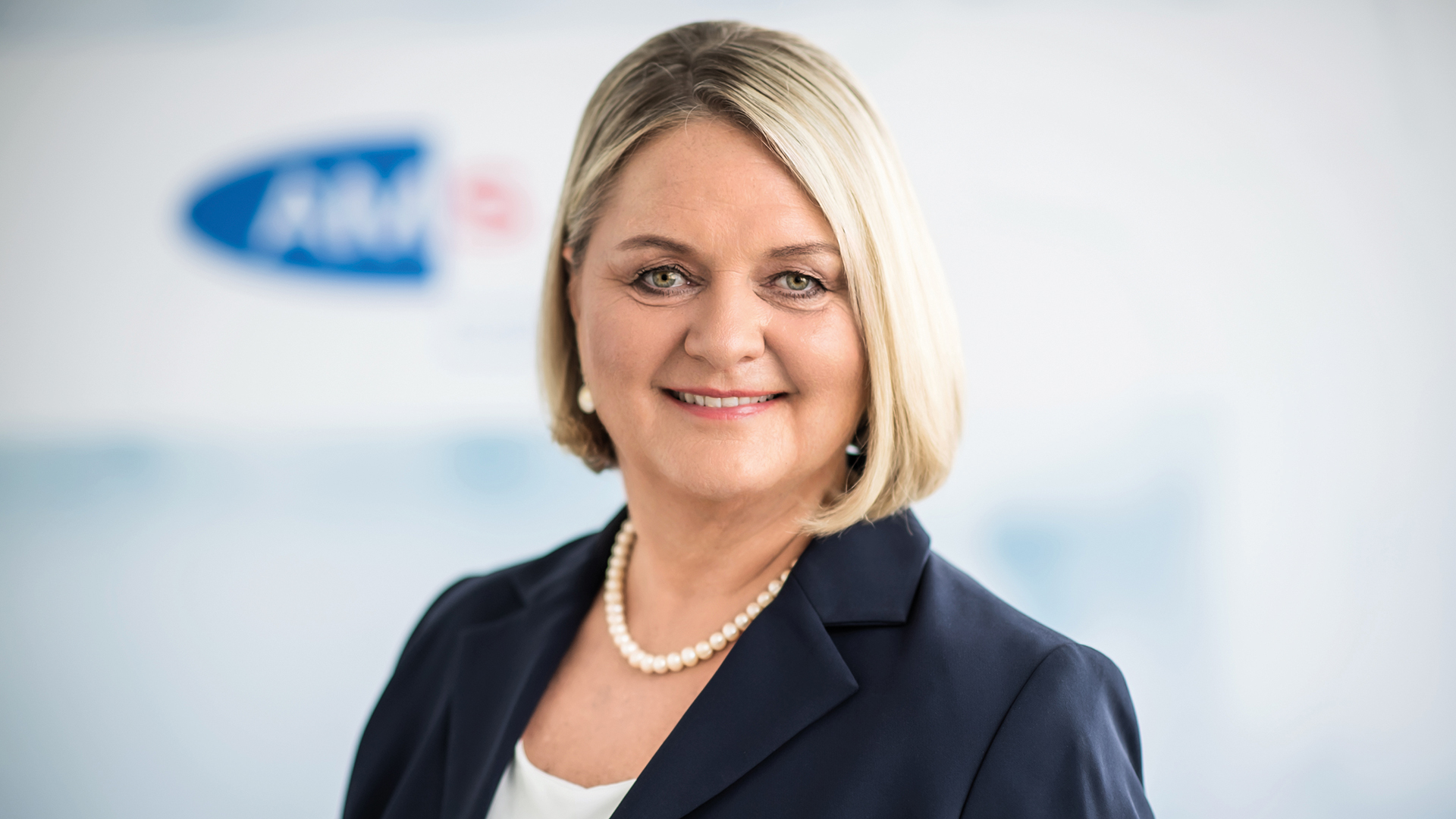 Helene Sengstbratl: Portrait einer blonden Frau mit dem AMS-Logo im Hintergrund