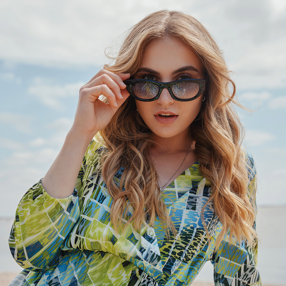 Blonde Frau schiebt sich gerade die schwarze Sonnenbrille von der Nase