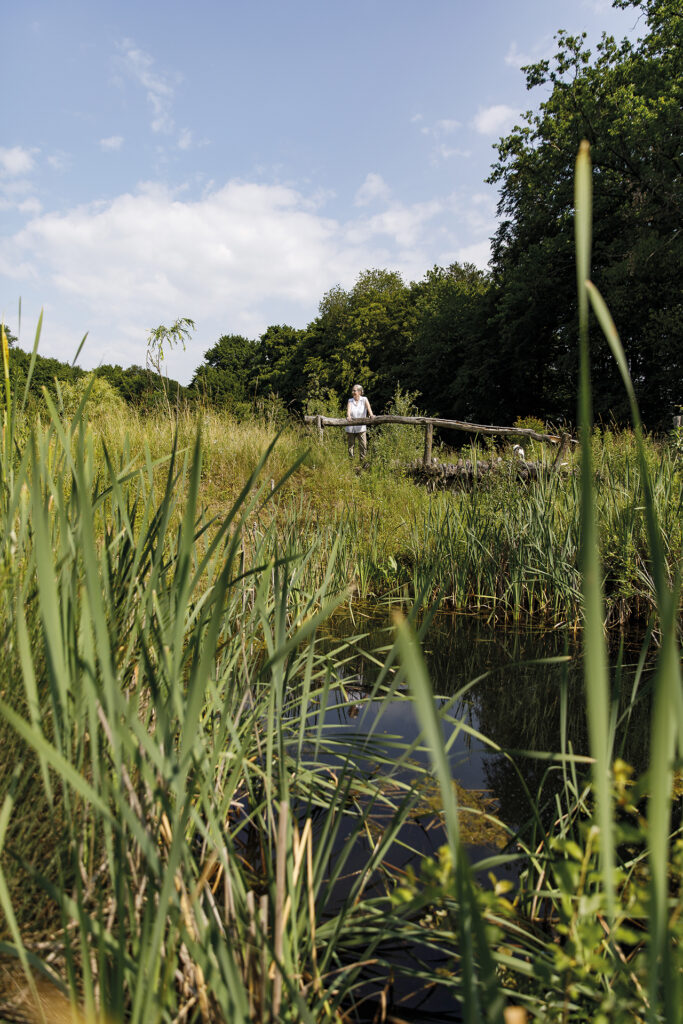 Frau lehnt an einer Holzbrücke über einem Teich
