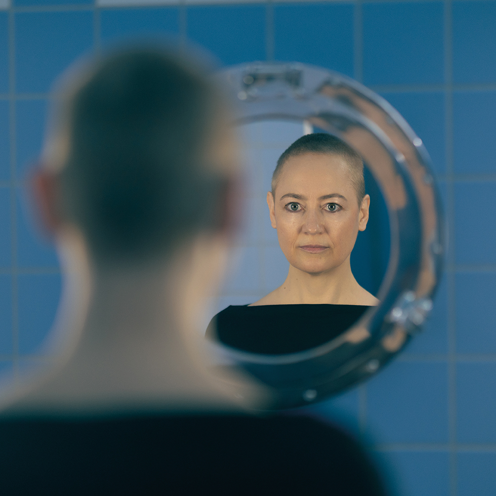 Eine Frau schaut in einen Spiegel im blau gefliesten Badezimmer