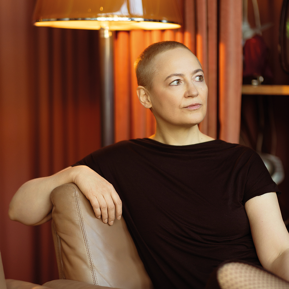 Petra Piuk: Frau mit sehr kurzen Haaren sitz nachdenklich auf einem Sofa