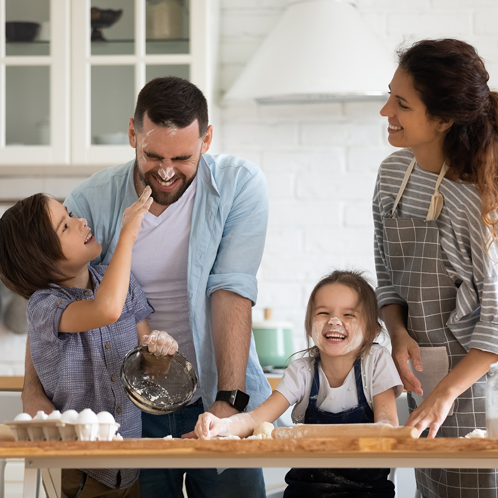 Überglückliche junge Familie mit kleinen Vorschulkindern hat gemeinsam Spaß beim Backen von Gebäck oder Kuchen zu Hause. Glückliche, lächelnde Eltern genießen das gemeinsame Wochenende mit ihren kleinen Kindern beim Backen in der Küche.