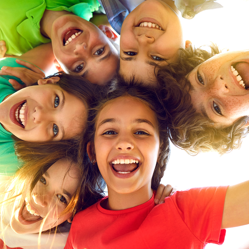 Eine Gruppe fröhlicher, niedlicher kleiner Kinder spielt gemeinsam und hat Spaß. Gruppenporträt glücklicher Kinder, die eng zusammenstehen, nach unten in die Kamera blicken und lächeln. Aufnahme aus der Froschperspektive – Freundschaftskonzept.