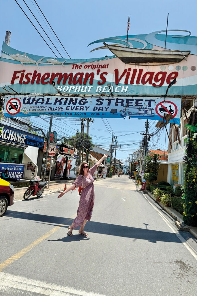 Thailand: Thailändische Straße – im Vordergrund eine glückliche Frau mit Sonnenbrille und langem Sommerkleid