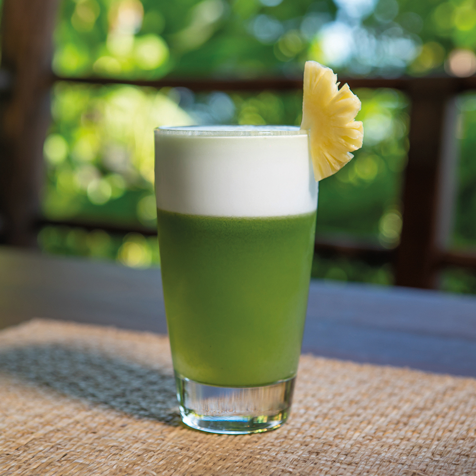 Detox: Grüner Smoothie im Glas mit Schaumkrone und Ananasscheibe am Rand.