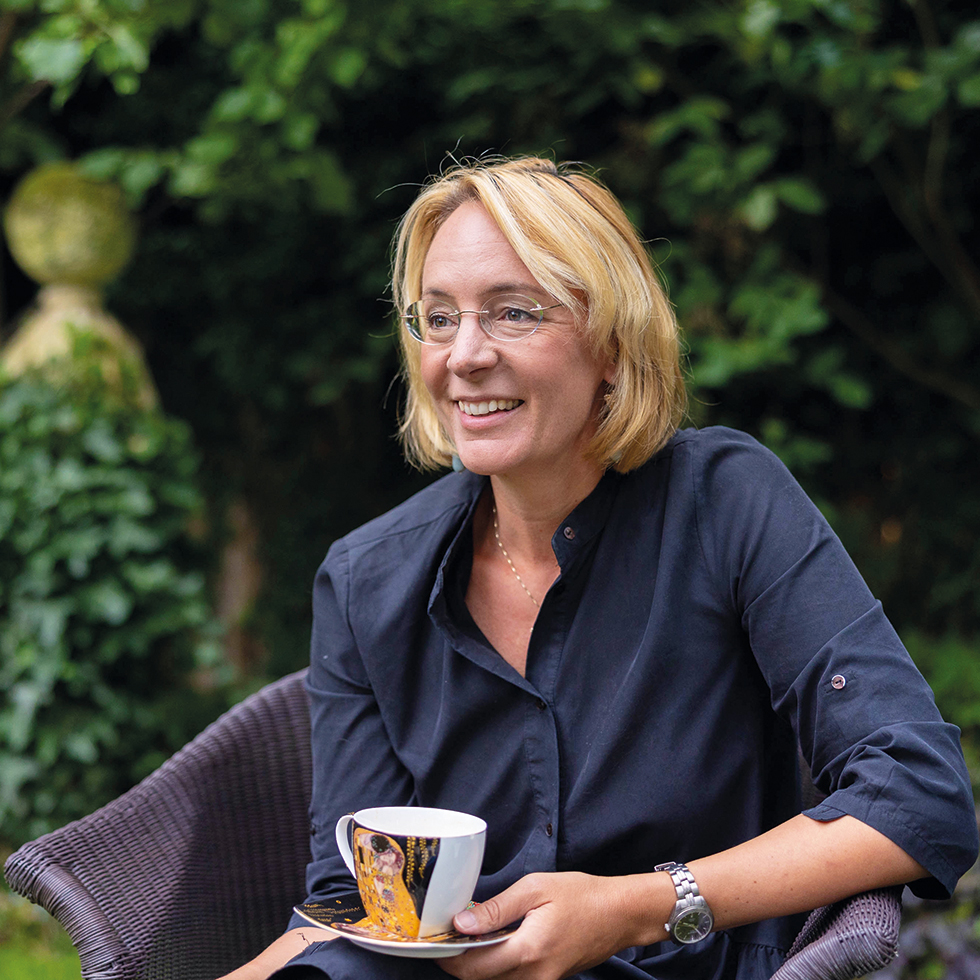 Sarah Spiekermann: Frau in dunkelblauem Kleid und Brille mit einer Teetasse mit Klimts Kuss in der Hand