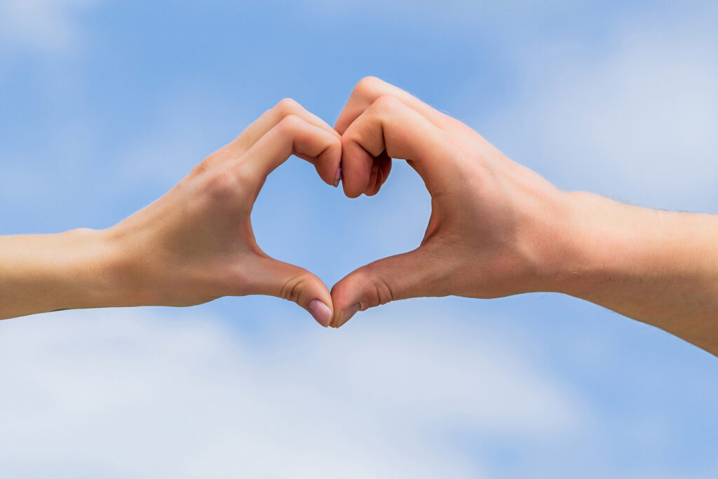 Frauen- und Männerhände in Herzform vor dem Himmel. Hände als Symbol der Liebe in Herzgestalt. Herz aus Händen mit Himmel im Hintergrund. Liebe, Freundschaft und Zuneigung. Weibliche und männliche Hand formen ein Herz vor blauem Himmel.