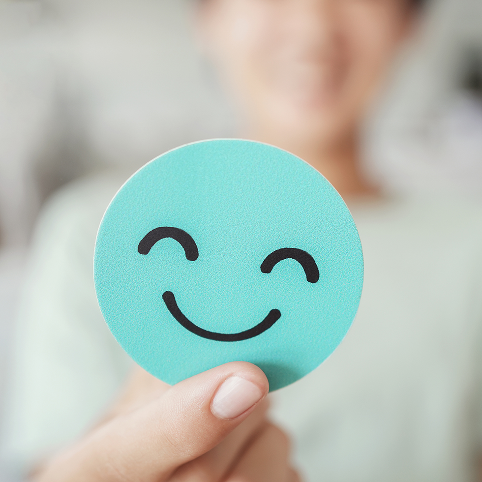 Dopamine Anchoring: Hände halten einen grünen Smiley aus Papier – Symbol für positives Denken, gute Bewertung, Feedback, Kundenrezension, Beurteilung, Kindergesundheit, Welttag der seelischen Gesundheit, Komplimenttag.