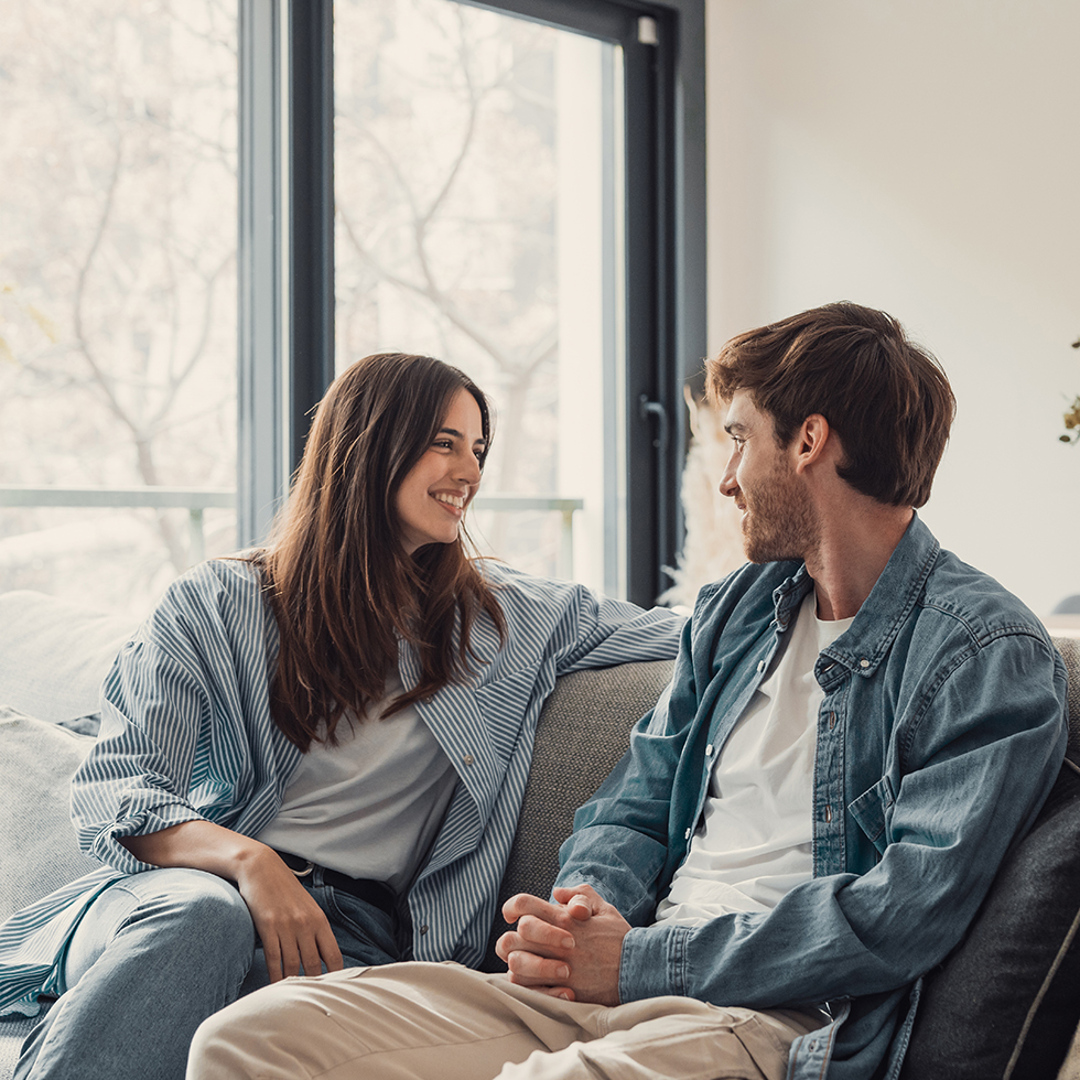 Junges, glückliches Paar hat Spaß, redet, lacht und entspannt sich zu Hause auf dem Sofa.