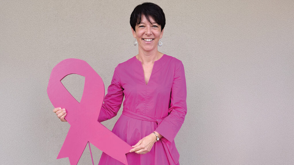 Pink Ribbon: Frau in pinkem Kleid hält eine große Pink-Ribbon-Schleife in den Händen