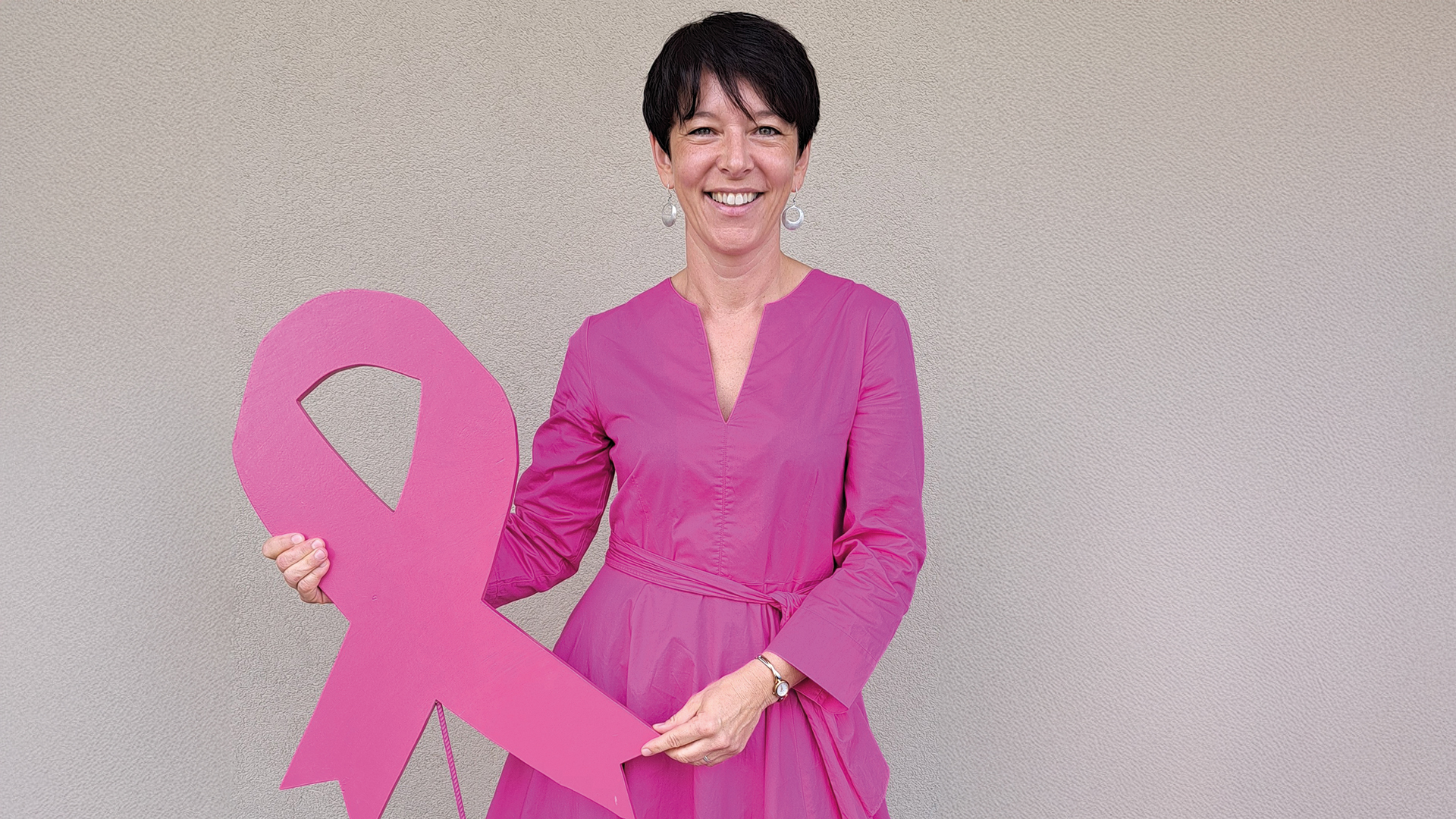 Pink Ribbon: Frau in pinkem Kleid hält eine große Pink-Ribbon-Schleife in den Händen