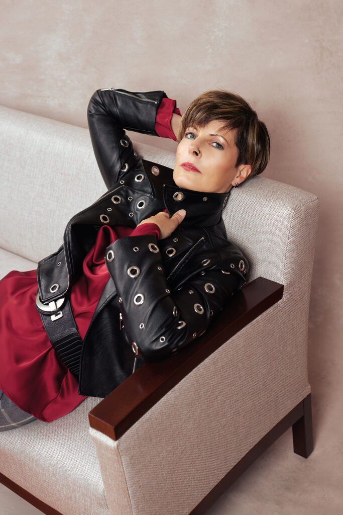 Gewinnerin des Covershootings 2025 – Kurzhaarige Frau mit Nasenring und Hand am Hinterkopf lehnt am Sofa