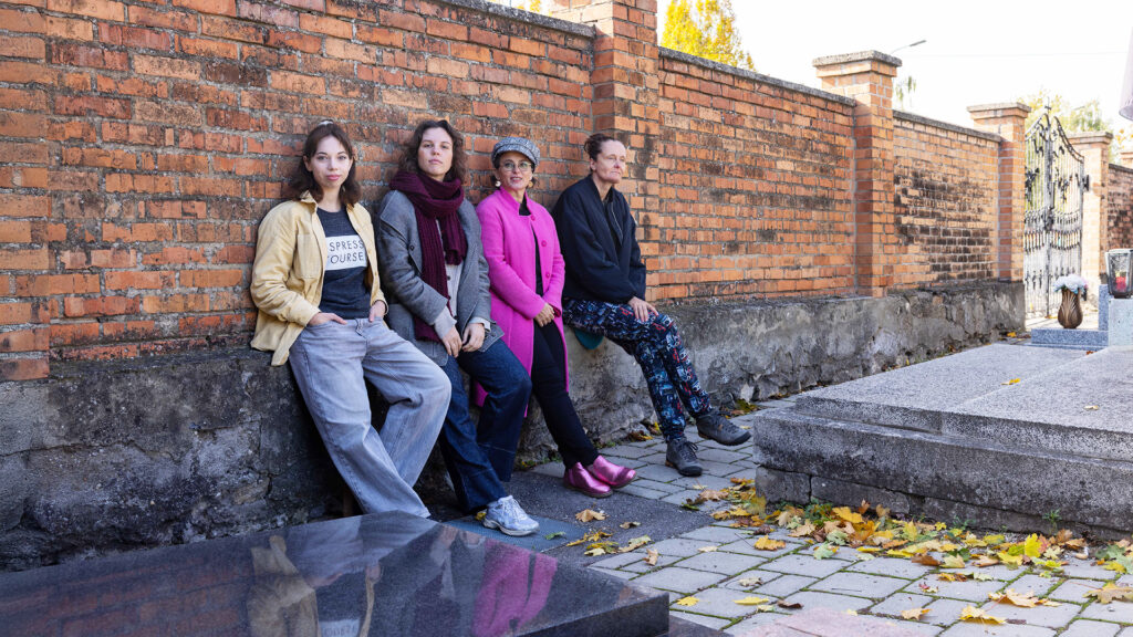 Vier Personen sitzen an einer Backsteinmauer auf einem Friedhof
