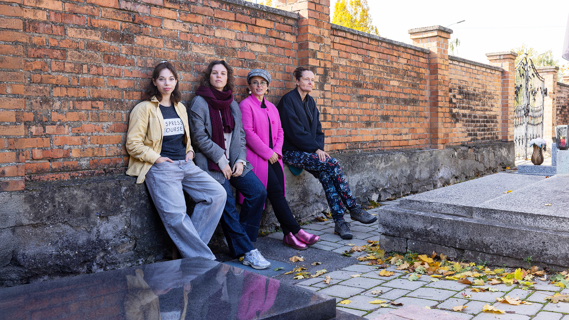 Vier Personen sitzen an einer Backsteinmauer auf einem Friedhof