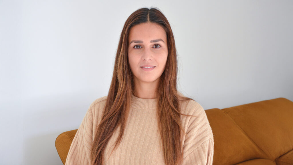 Katharina Bedenik: Porträt einer Frau mit langen braunen Haaren in beigem Pullover vor hellem Hintergrund