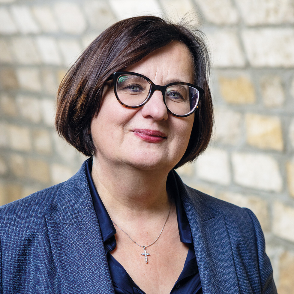 Dorothea Jagschitz: Porträt einer Frau mit Brille und Business-Outfit vor Steinmauer