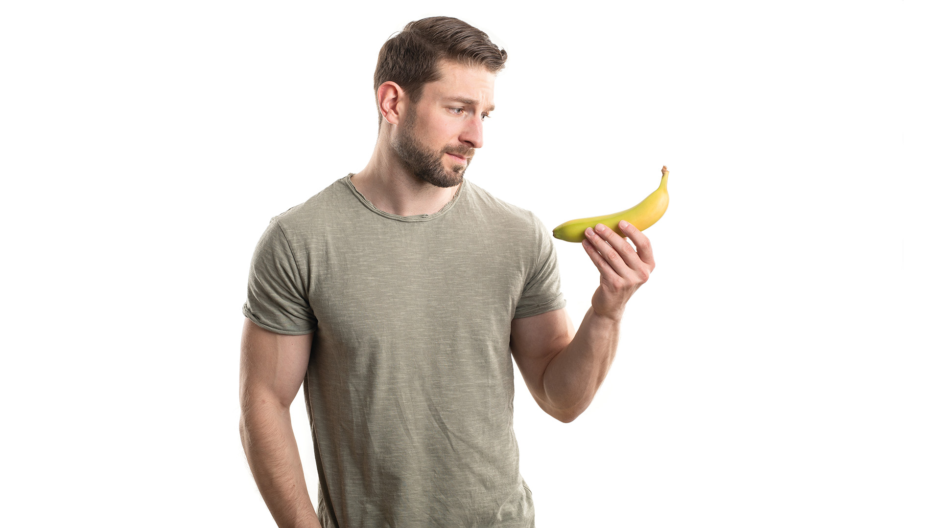 Penis: Attraktiver Mann mit Bart schaut skeptisch auf eine Banane