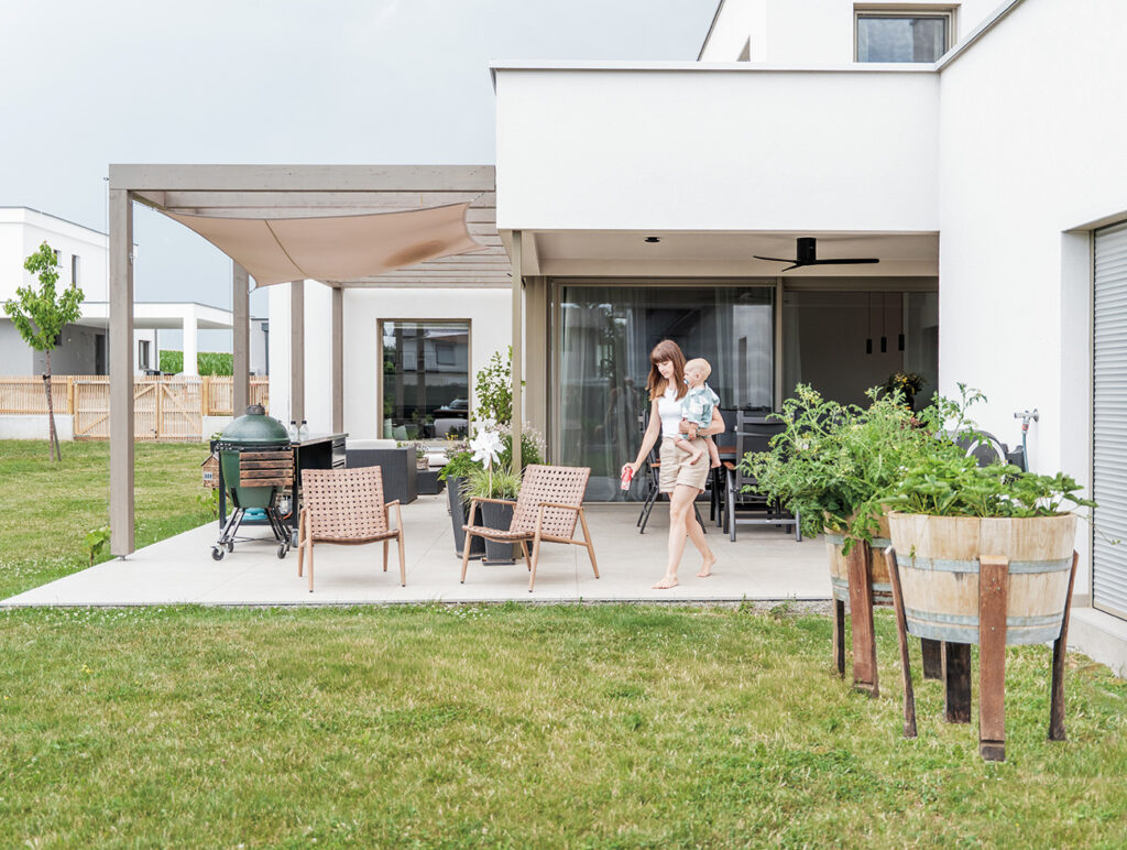 baderbau: Frau mit Kind auf moderner Terrasse mit Sitzbereich und Grill