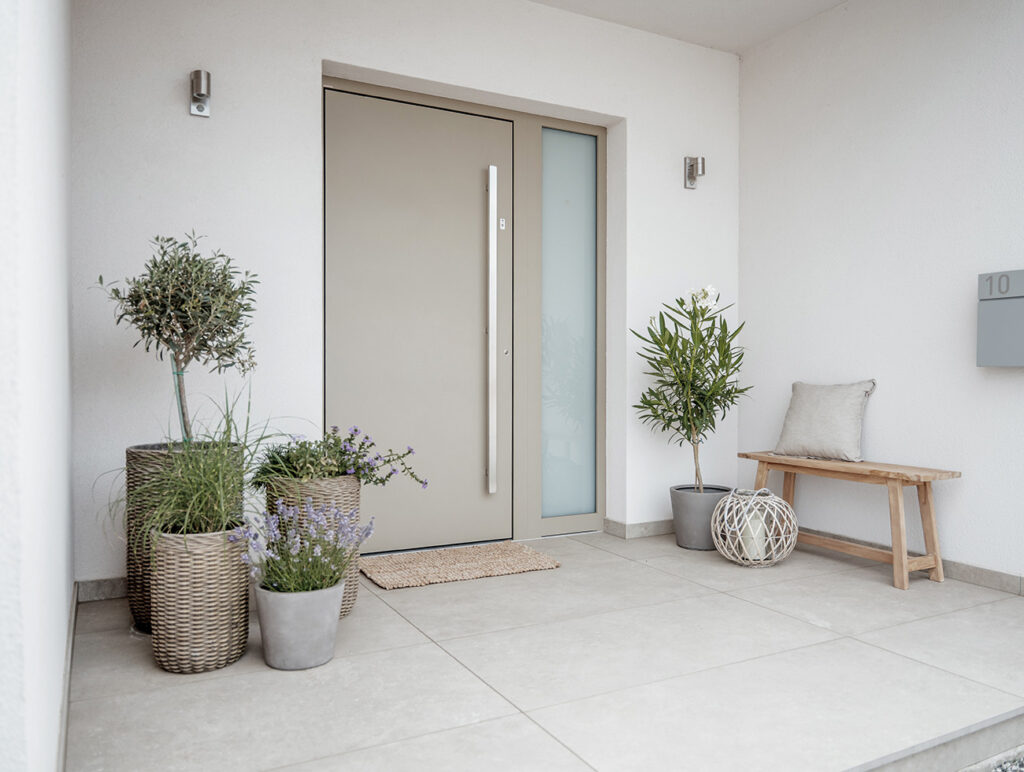 Einladender Hauseingang mit moderner Haustür, Sitzbank und dekorativen Pflanzenkübeln