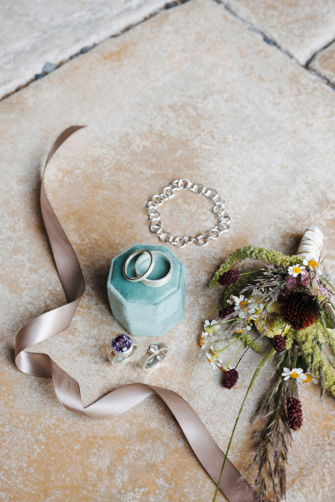 Silberne Eheringe, Armband und Blumenstrauß mit Wiesenblumen – stilvolle Hochzeitsdetails