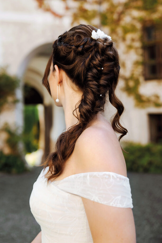 Brautfrisur mit geflochtenem Zopf, Perlen und Blütendetails – eleganter Hochzeitslook