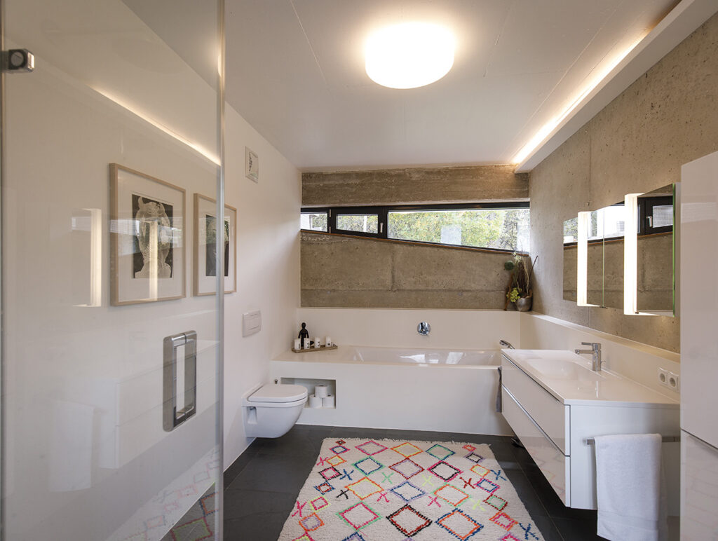 Modernes Badezimmer mit Betonwand, Badewanne und bunter Teppichdeko