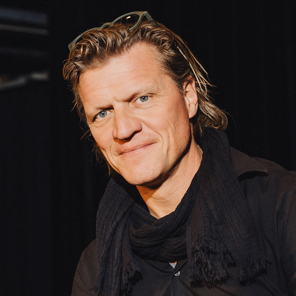 Gery Seidl: Porträt eines Mannes vor dunklem Hintergrund, trägt dunkles Hemd und Schal.