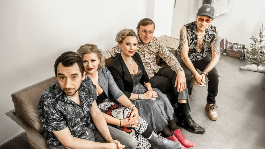 Fünf Personen sitzen gemeinsam auf einem Sofa in einem hellen Raum