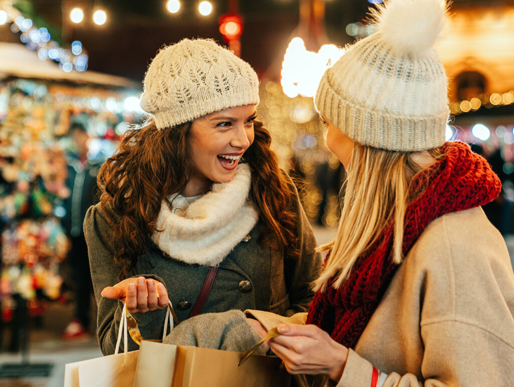 Adventmärkte: Zwei Frauen beim fröhlichen Weihnachtsshopping zwischen funkelnden Marktständen.