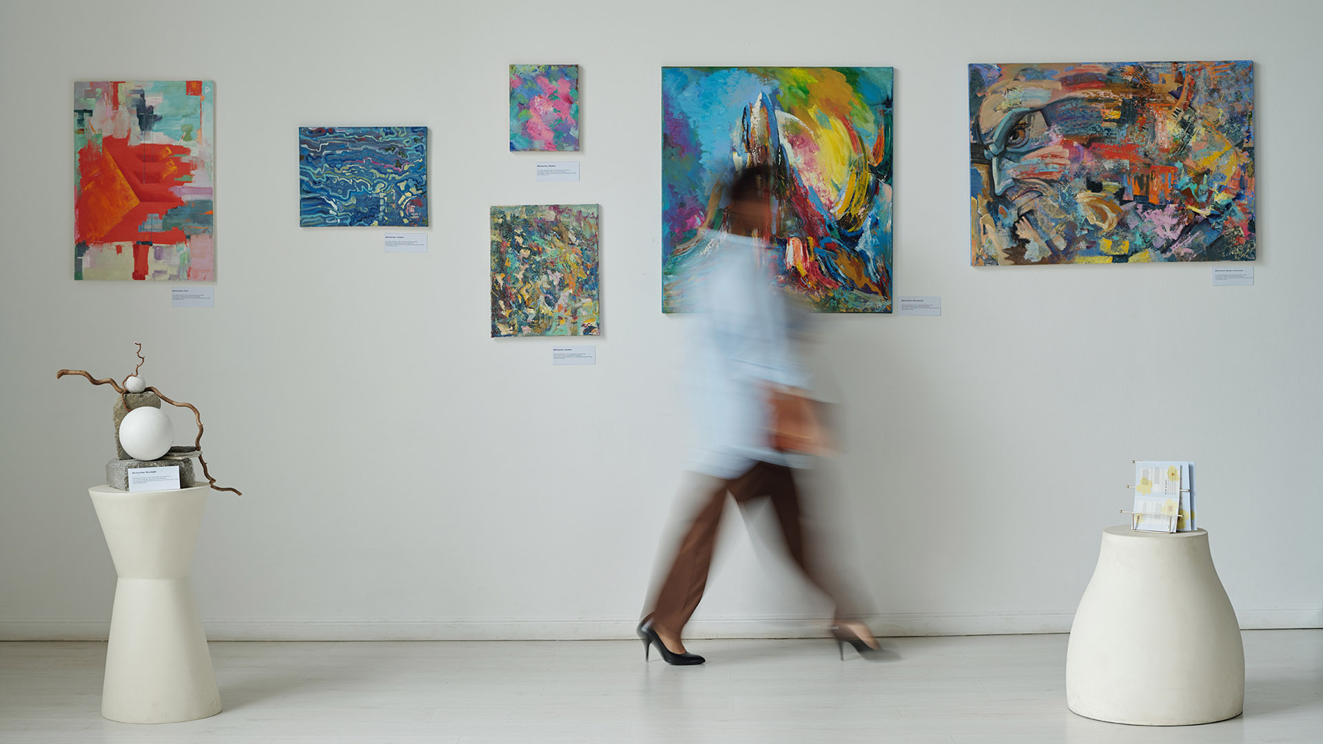 Kulturtipp: Verschwommene Bewegung einer jungen Frau, die an Gemälden an der Wand in einer Kunstgalerie vorbeigeht.