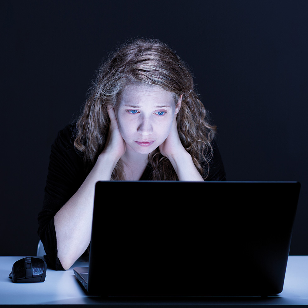 Frau sitzt nachts vor dem Laptop, schaut angespannt auf den Bildschirm.