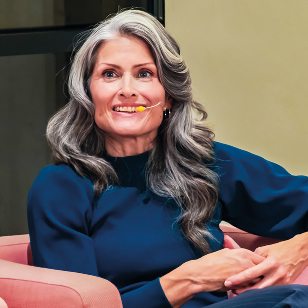 Podiumsdiskussion: Sprecherin mit langen grauen Haaren und Headset auf einem Sofa