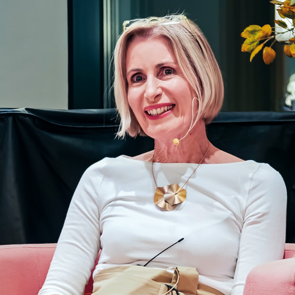 Podiumsdiskussion: Lächelnde Sprecherin mit blondem Bob und Headset im Gespräch