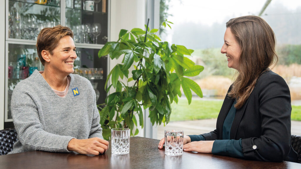 Michaela Dorfmeister: Zwei Frauen im Gespräch an einem Tisch vor großer Fensterfront.