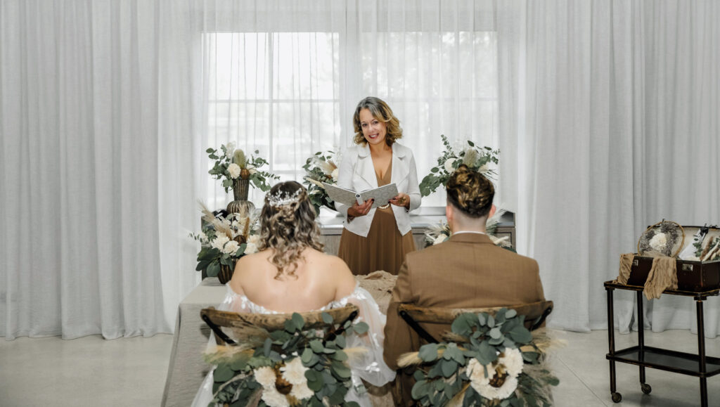 Hotel Nils: Eine Traurednerin traut ein Hochzeitspaar in einem hellen Raum.